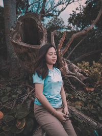 Young woman sitting on tree trunk in forest