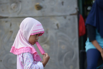 Cute girl licking ice cream by wall