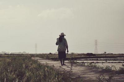 Rear view of mid adult man walking on dirt road against sky