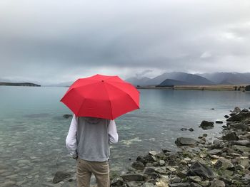 Rear view of teenage boy with umbrella while standing against lake