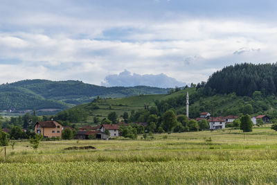 Scenic view of agricultural field by houses and mountains against sky