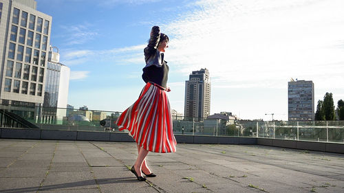 Happy woman wearing striped skirt and jacket on footpath in city