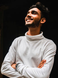 Young man looking away while standing against black background