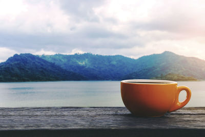 Coffee cup on table by mountains against sky