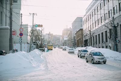 Cars on road by snow covered city against sky