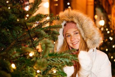 Smiling young girl in winter clothes in hood celebrates christmas on street