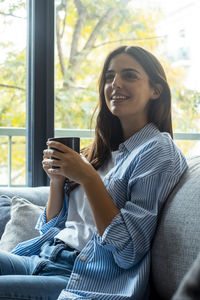 Young woman using mobile phone while sitting on sofa at home