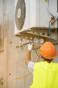 Rear view of electrician fixing pressure gauge on air conditioner