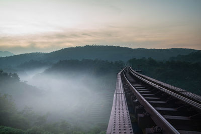 Railroad track and mountain against sky during sunset