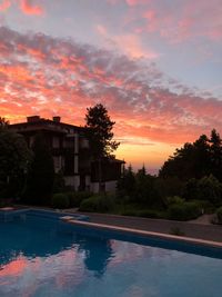 Swimming pool by trees against sky during sunset