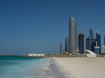 Modern buildings by sea against clear blue sky