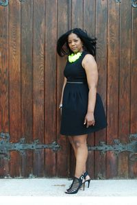 Full length portrait of woman standing against wooden door