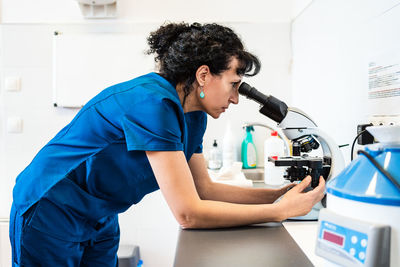 Female doctor looking through modern microscope placed on table in lab of modern clinic