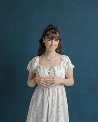 Portrait of young woman standing against blue background