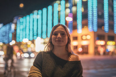 Portrait of smiling woman standing on illuminated street in city at night