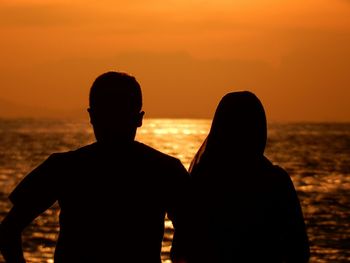 Silhouette couple standing at beach against orange sky during sunset