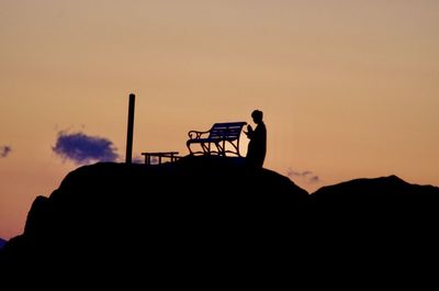 Silhouette people sitting on mountain against sky during sunset