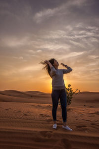 Young woman standing on sand against sky during sunset