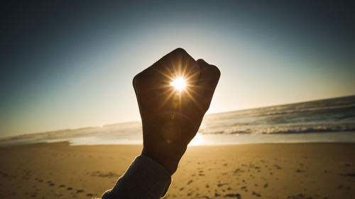 Hand holding sun shining over sea against sky during sunset