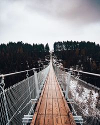 Footbridge in forest against sky