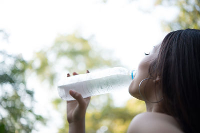 Young woman drinking water while standing outdoors