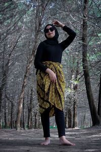 Portrait of man standing by tree trunk in forest
