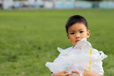 Portrait of cute boy collecting garbage in plastic bag on field