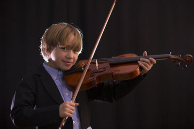 Boy playing violin while standing against black background