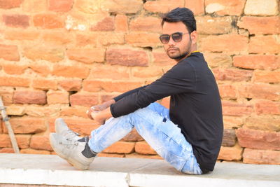 Young man looking away while standing against wall