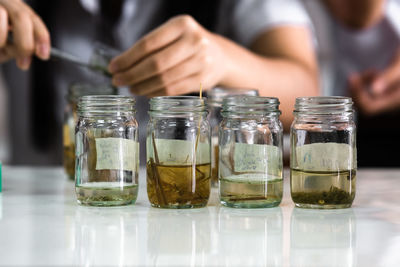 Cropped image of person holding glass of jar on table