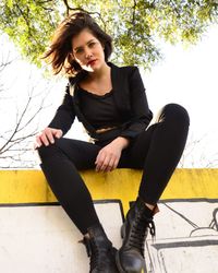 Low angle portrait of young woman sitting on railing against clear sky