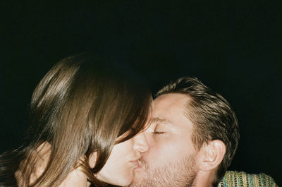 Close-up of affectionate couple kissing against black background