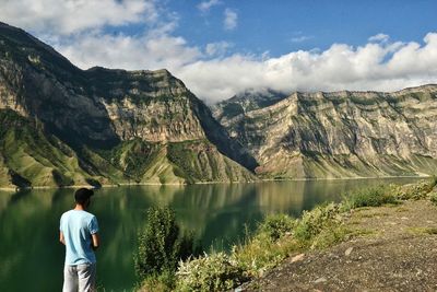 Rear view of man standing by lake against mountains