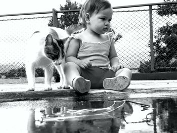 Cute girl sitting with cat by puddle