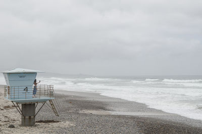 Side view of young woman taking selfie while standing on lifeguard hut at beach