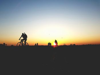 Silhouette people riding bicycle against sky during sunset