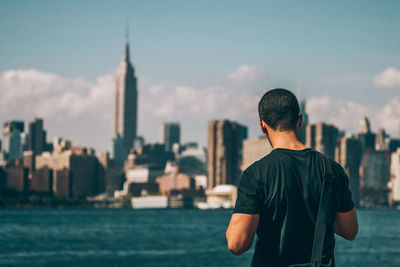 Rear view of man standing by sea against manhattan