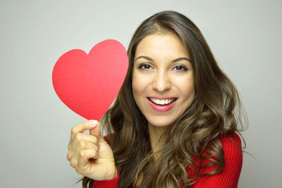 Portrait of smiling young woman holding heart shape over white background