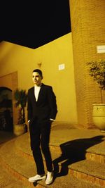 Portrait of young man standing against wall in city