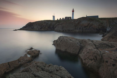 Rocks by sea against sky during sunset