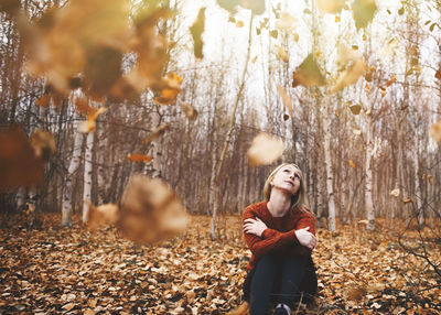 Young woman looking away while standing on tree trunk in forest