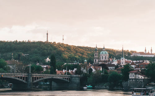 Bridge over river by buildings in city against sky