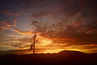 Silhouette electricity pylons against sky during sunset