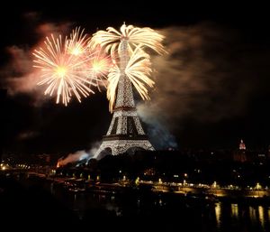 Low angle view of firework display over river against sky