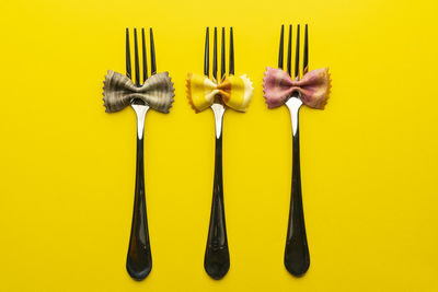 Three forks with pieces of pasta with the shape of a colored butterfly on a yellow surface