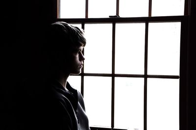 Thoughtful young man looking though window at home