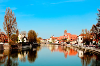 Buildings by river against blue sky