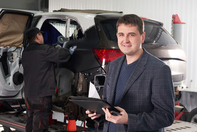 Portrait of businessman standing while mechanic working in background