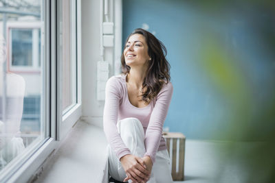 Happy woman sitting beside window sill looking out of window