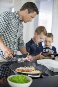 Father looking at sons using digital tablet while preparing food in kitchen